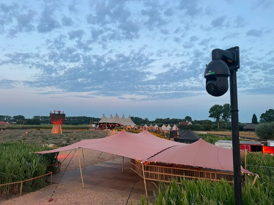 Een festivalterrein bij valavond Festivalterrein bij schemering met stretchtenten en een PTZ camera van EventWiFi op een mast